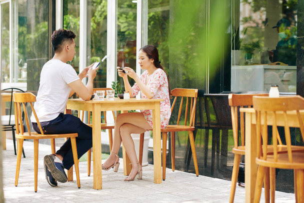 Genç Asyalı çift dışarıda kafede kahvaltı ederken sosyal medyayı kontrol ediyor ve arkadaşlarına mesaj atıyor. - Fotoğraf, Görsel