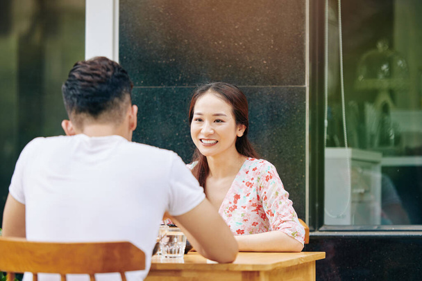Улыбающаяся молодая вьетнамская женщина, встречающаяся с парнем за столиком кафе
 - Фото, изображение