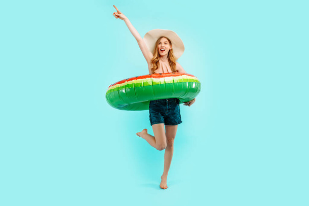 Full length, excited happy girl dressed in a swimsuit and a summer cap, having fun and celebrating the victory with an inflatable swimming circle on a blue background - Foto, Imagem