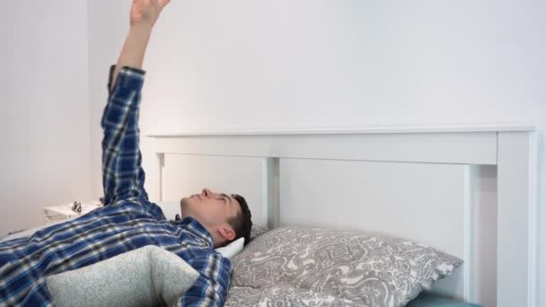 Nezaměstnaný mladý pohledný bělošský bruneta muž nosí modrou kostkovanou flanelovou košili, leží sám na šedé posteli, dívá se do stropu, zvrací a chytá žlutý tenisový míček doma. Koncept nečinnosti. Vnitřní - Záběry, video
