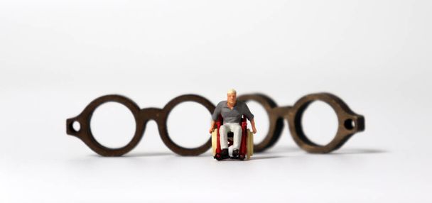 Мініатюрна людина в інвалідному кріслі перед двома дерев'яними мініатюрними окулярами
. - Фото, зображення