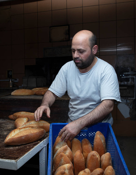 Fırında çalışan genç bir erkek işçi. O, ekmeği rafa koyar. Fırından taze somun ekmeği. Ekmek pişiriyorum. Fırın Taşımacılığı. - Fotoğraf, Görsel