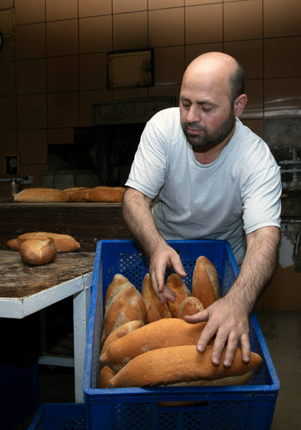 Fırında çalışan genç bir erkek işçi. O, ekmeği rafa koyar. Fırından taze somun ekmeği. Ekmek pişiriyorum. Fırın Taşımacılığı. - Fotoğraf, Görsel