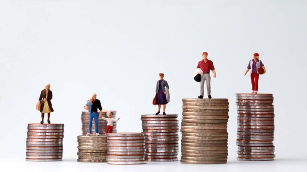 Miniature people standing on piles of different heights of coins. The concepts of person and wealth. - Foto, Imagen