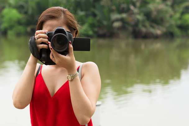 Lady macht ein Foto in der Natur in der Nähe des Wassers, mit Blick in die Kamera. Porträt. Fotografie. - Foto, Bild