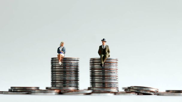 Un hombre en miniatura y una mujer en miniatura sentados en una pila de monedas de la misma altura
. - Foto, imagen