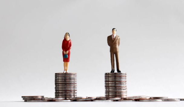 Miniaturowy mężczyzna i miniaturowa kobieta stojąca na stosie monet tego samego wzrostu. - Zdjęcie, obraz