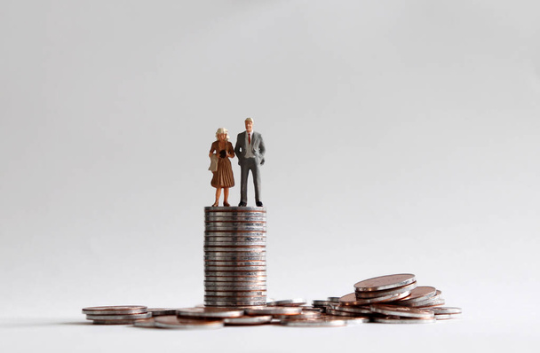 Ein Mann und eine Frau im Miniaturformat stehen auf einem Haufen Münzen. - Foto, Bild