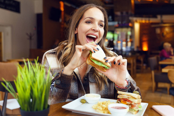 サイドビューポートレート白人女性はレストランで日にサンドイッチを食べる - 写真・画像