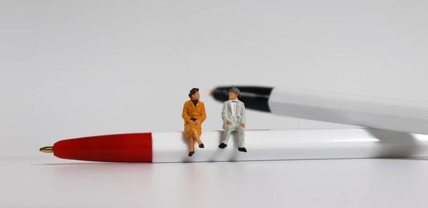 A miniature old couple sitting on a red ballpoint pen with a black ball pen. - Photo, Image