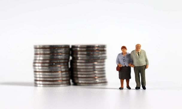 Miniaturní starý pár stojící vedle hromady mincí. - Fotografie, Obrázek