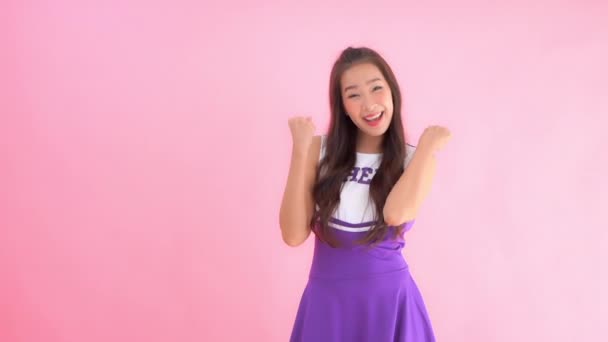 záběry krásné asijské ženy v fialové roztleskávačky šaty na růžovém pozadí - Záběry, video