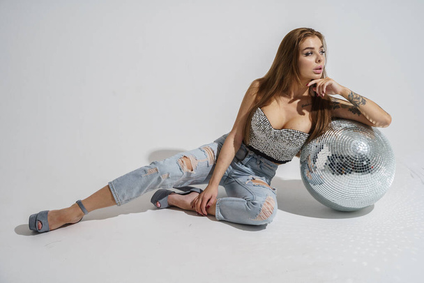 Elegante morena con bola disco posando en el estudio sobre fondo gris
   - Foto, Imagen