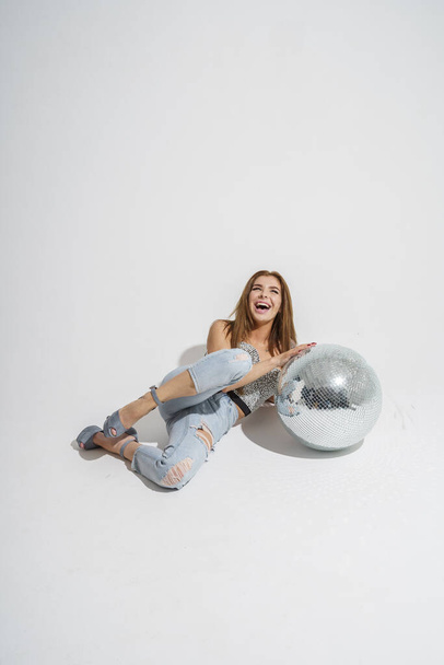 Stylish brunette with disco-ball posing at studio on gray background   - 写真・画像