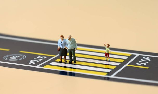 Una pareja de ancianos en miniatura y un niño en miniatura cruzando un paso de peatones
. - Foto, imagen