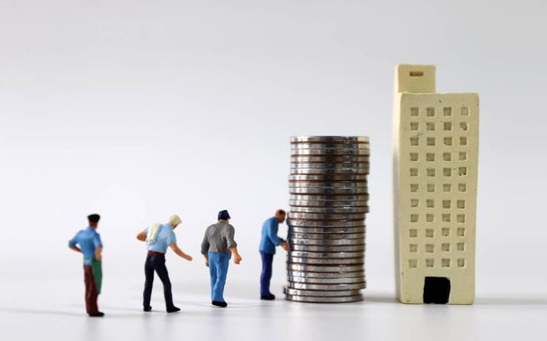 Miniature people lining up in front of buildings and piles of coins. - Photo, Image