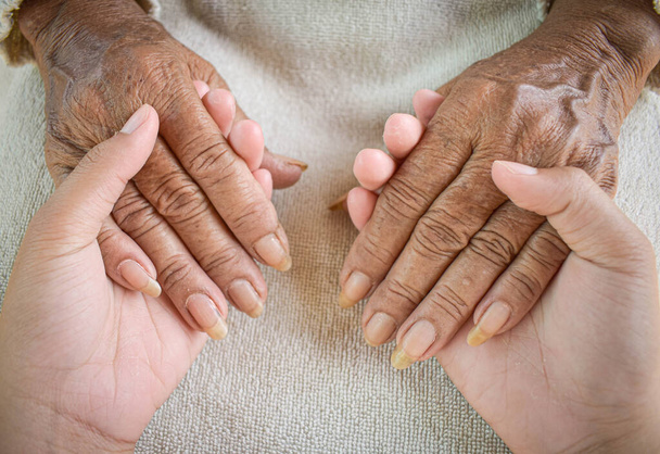 lähikuva tyttärentytär huolehtii terveydentilasta sairaasta isoäidistä kotona pitämällä kädestä. Elämäntapa tukee perheen rakkautta. - Valokuva, kuva