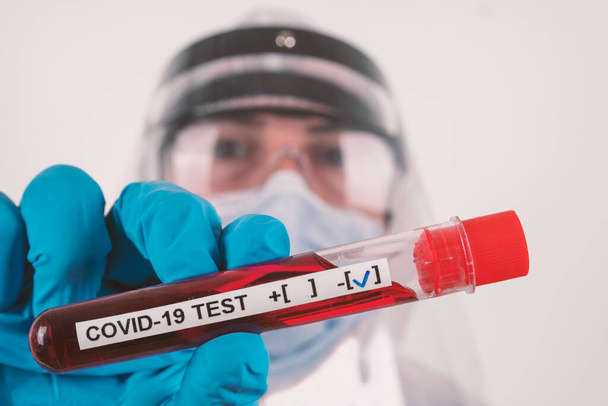 Concept de test sanguin du virus Corona : Un travailleur de laboratoire avec masque de protection, gants bleus et lunettes tient une éprouvette sanguine avec résultat NEGATIVE COVID-19. - Photo, image