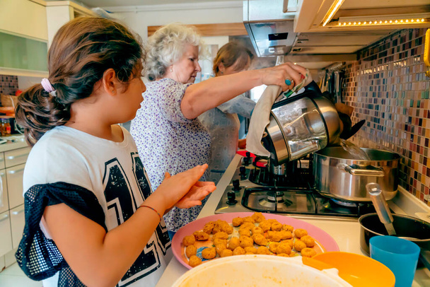 Μαγειρική τριών γενεών: Η Τουρκάλα γιαγιά διδάσκει στο εγγόνι της παραδοσιακή κουζίνα της Μέσης Ανατολής. Κορίτσι που ετοιμάζει μπάλες φακής. Ηλικιωμένο βραστό νερό. Μητέρα στο φόντο της κουζίνας - Φωτογραφία, εικόνα