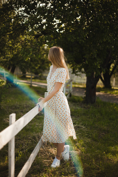 Dívka v bílých šatech kráčí v přírodě. Blondýna v pohybu na farmě. Mladá dívka si užívá léta. - Fotografie, Obrázek