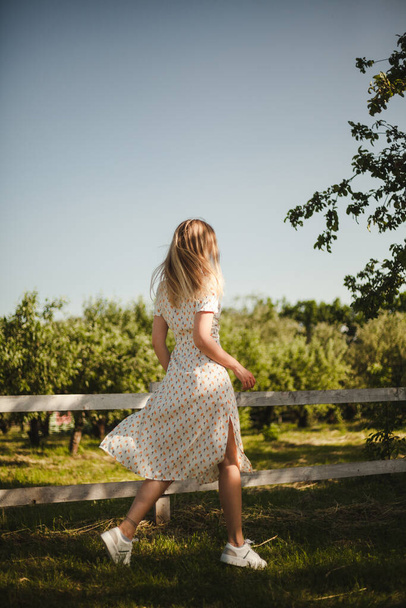Chica en un vestido blanco caminando en la naturaleza. Rubia en movimiento en una granja. Una jovencita disfruta del verano
. - Foto, Imagen