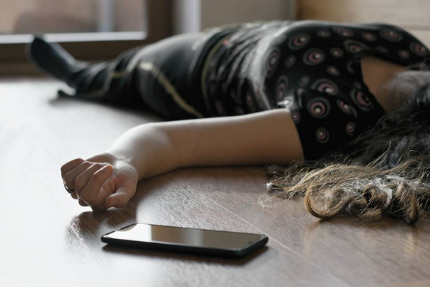 Γυναίκα ξαπλωμένη στο πάτωμα στο σπίτι, το τηλέφωνο έπεσε κοντά στο χέρι της. - Φωτογραφία, εικόνα