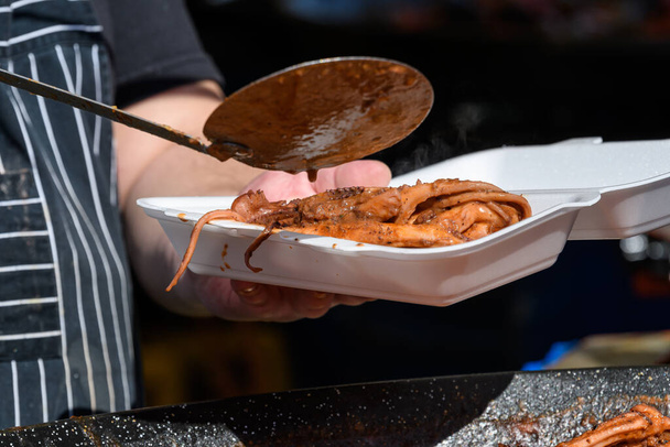 Pişirilmiş ahtapot ve domates sosu, deniz ürünleri yemeye hazır bir sokak yemeği festivalindeki paket kutusuna aktarılıyor. - Fotoğraf, Görsel