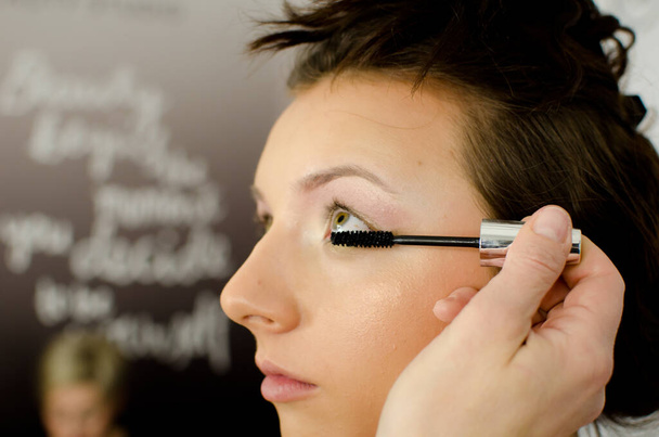 Visagistin trägt schwarze Wimperntusche mit Pinsel auf die Augen auf. Schöne Frauenaugen Make-up. Seitenprofil der schönen jungen Frau Studioaufnahme,  - Foto, Bild