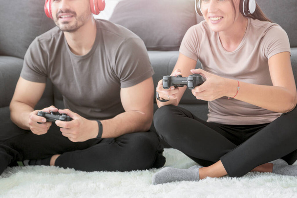 Feliz pareja alegre divirtiéndose jugando videojuegos en casa, los jóvenes sentados en el piso de la sala de estar y usando el joystick de consola juntos juegan juego, los jóvenes descansando en casa
 - Foto, Imagen