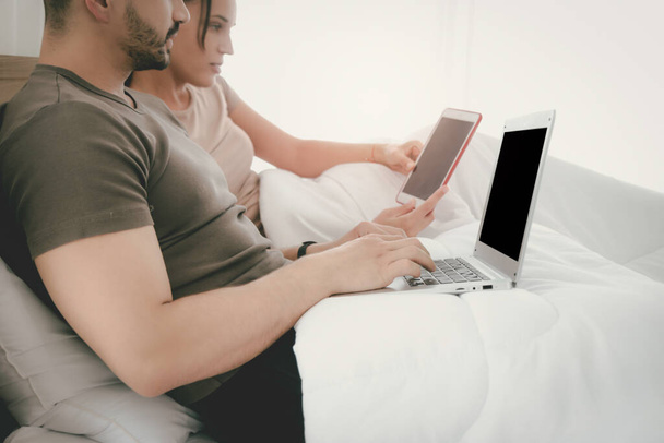 Couple working from bedroom, man using laptop computer, woman using digital tablet during lying on bed, searching information and online shopping, social media for online business, work form home - Photo, Image