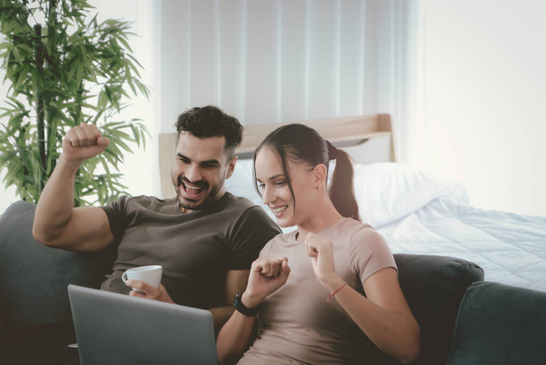 Happy couple raise hand during work on laptop computer at home, search online information and shopping, young people use social media for business online meeting, new normal work form home concept - 写真・画像