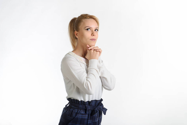 vista lateral de uma menina loira de 20 anos em blusa branca e saia azul no fundo branco pensando em algo
 - Foto, Imagem