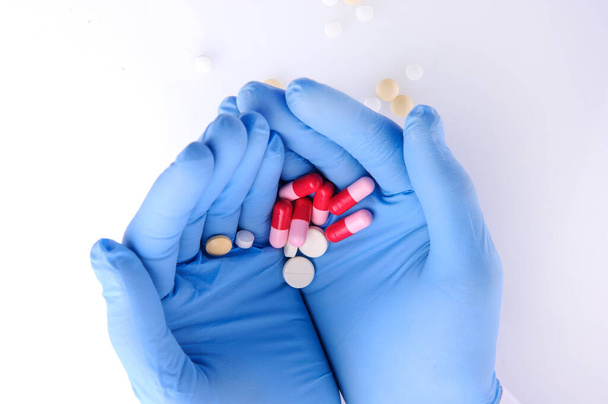 the hands of a doctor in blue gloves holding pills of different color  - Fotoğraf, Görsel