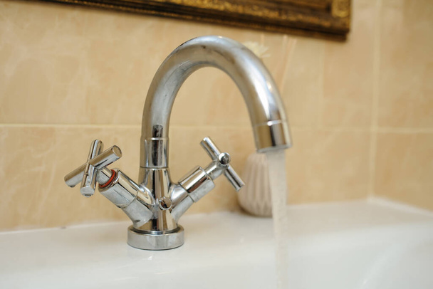 срібний змішувач з краплями води на білій раковині в красивій ванній кімнаті
 - Фото, зображення