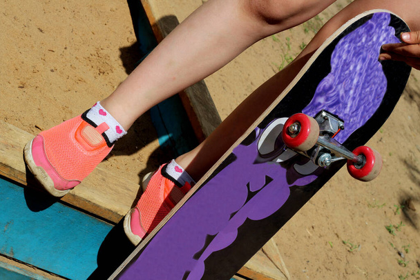 Meisje met roze sneakers en een skateboard. Voeten op een skateboard, zonlicht. - Foto, afbeelding