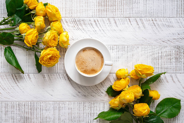 Cup of coffee and yellow roses on white wooden table. Top view. Flat lay. - Foto, immagini