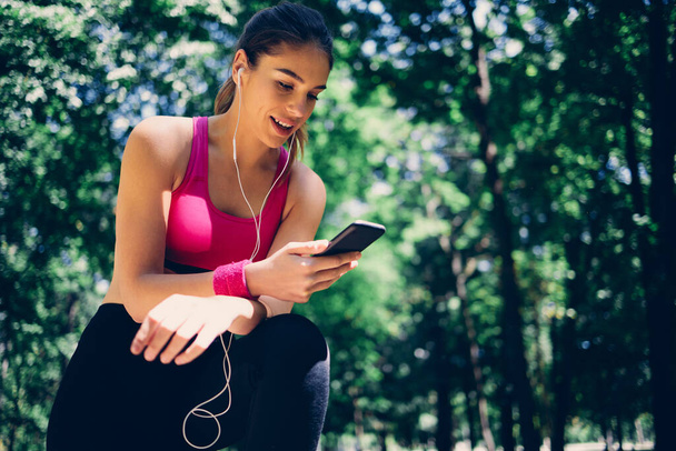 Mladý atraktivní běloch usmívající se žena běžec dává si pauzu od běhu a pomocí chytrého telefonu. - Fotografie, Obrázek