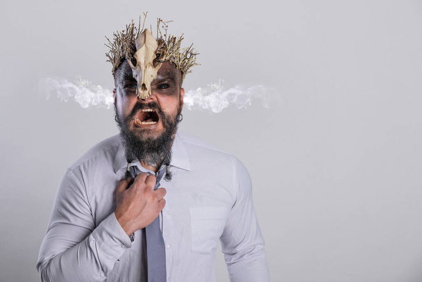 Concept of stress at work with smoke from his ears. Screaming viking warrior with crown skull straightens the tie that strangles him - Photo, Image