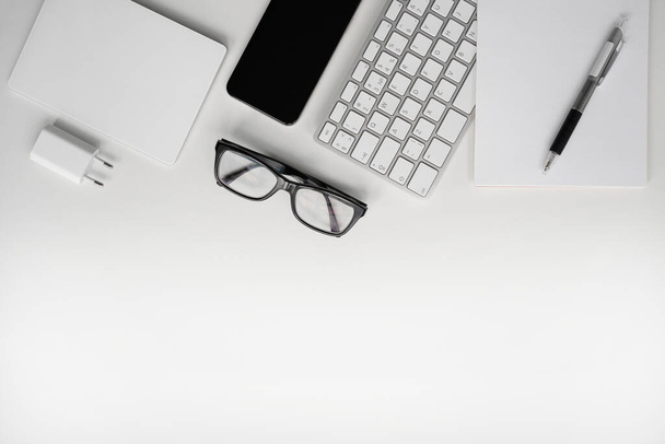 White workplace. Mobile phone, keyboard, touchpad, pen, notebook, charger and glasses. Copy space.  - Foto, Bild