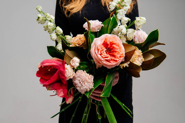 Bouquet of flowers in the hands of red-haired girl florist on light background. Rose, amaryllis, eustoma, delphinium, magnolia leaves. - Zdjęcie, obraz