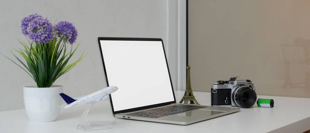 Reisevorbereitungskonzept mit Laptop-Attrappe, Kamera, Reisezubehör und Dekoration auf weißem Arbeitstisch in Seitenansicht - Foto, Bild