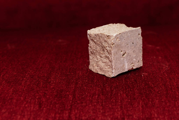 Cubo de piedra áspera aislado sobre fondo rojo borroso; enfoque en piedra
 - Foto, imagen