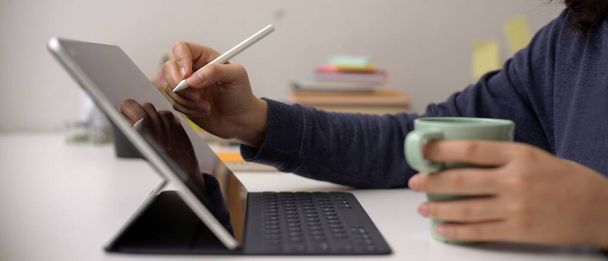 Oldalnézet női alkalmazott írás digitális táblagépen Stylus toll és a kezében kávésbögre az irodai asztalon  - Fotó, kép