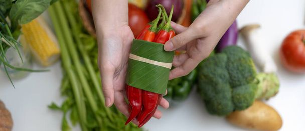 Close up view of hands holding red chili pepper while standing at table with other fresh farm vegetables - Foto, Imagen