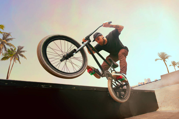 BMX rider is performing tricks in skatepark on sunset. - Fotó, kép