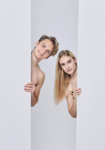 young man and girl stand behind white billboards. showing signs of attention to each other. the concept of advertising, psychology of relationships. white back - Foto, afbeelding