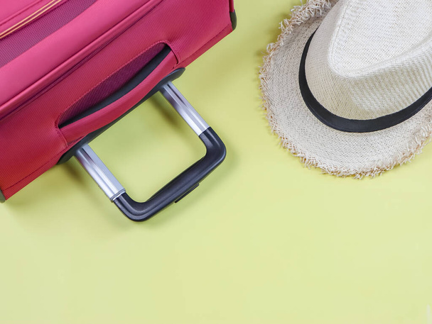 Seyahat konsepti, seyahat aksesuarlarının üst görünümü, pembe bavul sapı ve sarı arka planda fotokopi alanı olan şapka. - Fotoğraf, Görsel