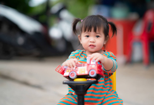 χαρούμενο κορίτσι παιδί με ένα παιχνίδι αυτοκινήτου, χαριτωμένο παιδί που παίζει σε εξωτερικούς χώρους. - Φωτογραφία, εικόνα