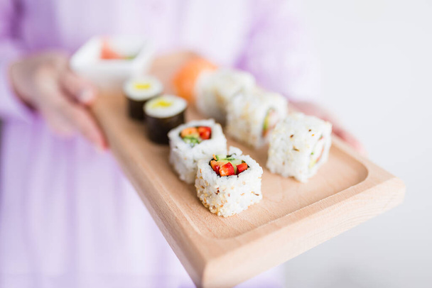 Close up of woman holding wooden platter sushi set. Japanese restaurant concept. - 写真・画像