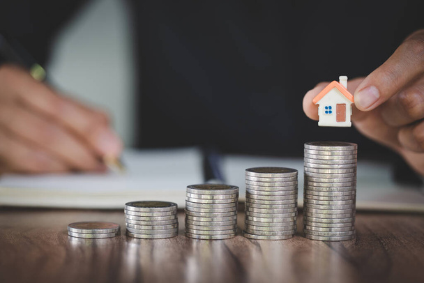Woman hand hold a  home model put on the stack coin with growing, Savings money for buy house and loan to business investment for real estate concept. Invesment and Risk Management. - Φωτογραφία, εικόνα